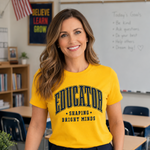 A woman wearing a bright yellow graphic t-shirt with 'EDUCATOR SHAPING BRIGHT MINDS' printed in dark green and black, standing in a classroom setting.