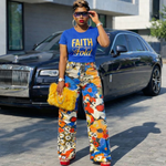 Woman wearing a blue 'FAITH don't FOLD' t-shirt and colorful pants in front of a black car.