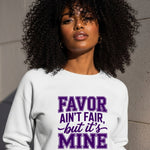 Woman wearing a white sweatshirt with purple text against a gray wall.