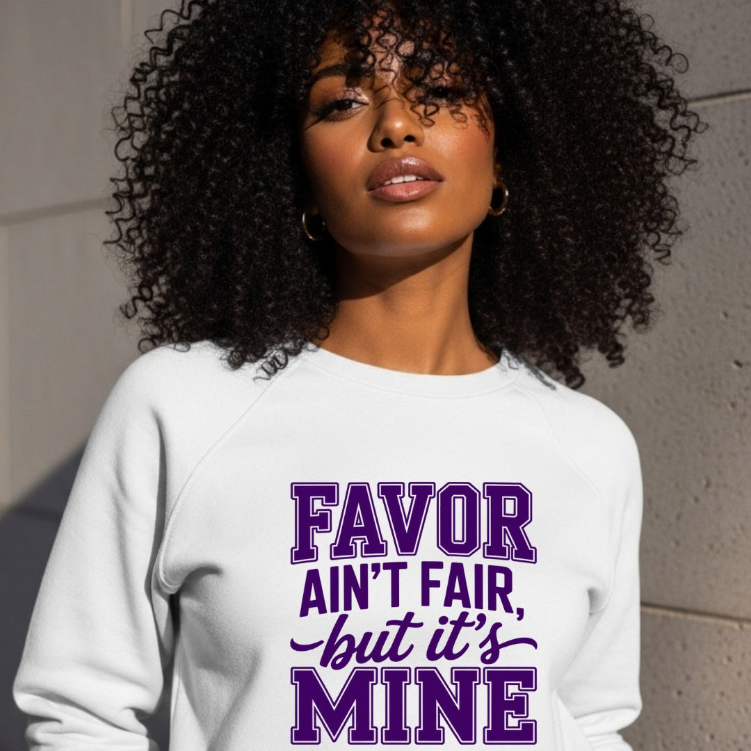 Woman wearing a white sweatshirt with purple text against a gray wall.