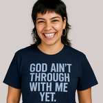 Person wearing a navy blue t-shirt with 'GOD AIN'T THROUGH WITH ME YET.' text on a plain background