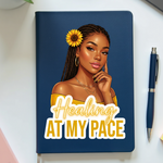 Notebook with a design of a woman with a sunflower and 'Healing at My Pace' text on a white surface.