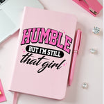 Pink JOURNAL with 'Humble but I'm still that girl' text on a pink surface