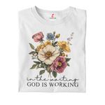White t-shirt with floral design and text 'In the waiting God is working' on a white background