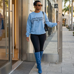 Woman in a blue sweater and blue boots standing outside a building.