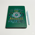 Green notebook with 'I'm proof that God answers prayers' text and a pen on a light gray background