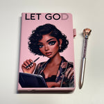Notebook with a cover featuring an illustration of a woman and the text 'LET GOD' on a pink background, accompanied by a pen.