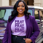 Woman wearing a purple blazer and 'Pray on it' t-shirt standing in front of a vehicle.