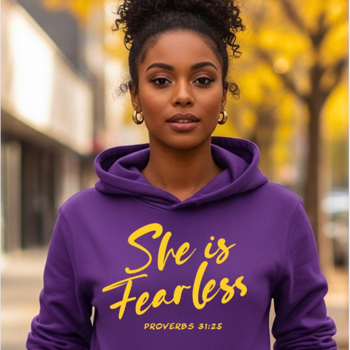 Woman wearing a purple hoodie with 'She is Fearless' text in yellow, standing outdoors.