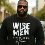 Man wearing a black sweatshirt with 'WISE MEN STILL SEEK HIM' text, standing outdoors.