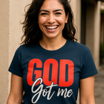 Woman wearing a navy t-shirt with 'GOD Got me' text, standing outdoors.