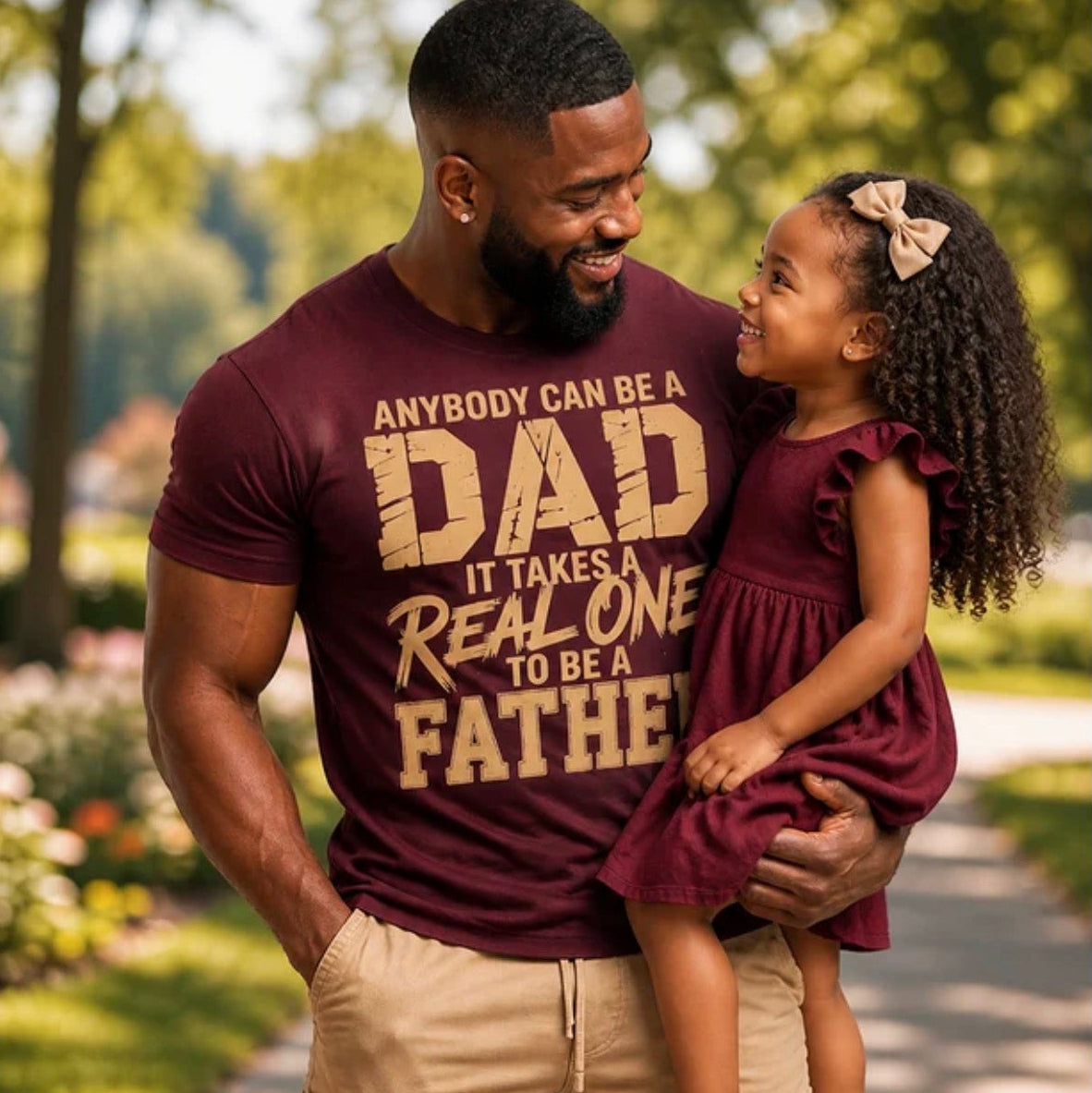 Man wearing a t-shirt with a fatherhood message, holding a young girl outdoors.