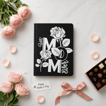 Black notebook with 'Best Mom Ever' design surrounded by pink roses and chocolates on a light surface.