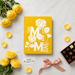 Yellow notebook with 'Best Mom Ever' text, surrounded by yellow roses and chocolates on a light background.