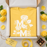 Yellow t-shirt with 'Mom' and rose design in a box, surrounded by yellow roses and a 'Happy Mother's Day' tag.