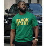 Man wearing a green 'Black Luxury' t-shirt standing in front of a black SUV.