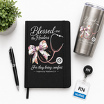 Black notebook with 'Blessed are the Healers' design, tumbler, pen, and nurse badge holder on a white surface.