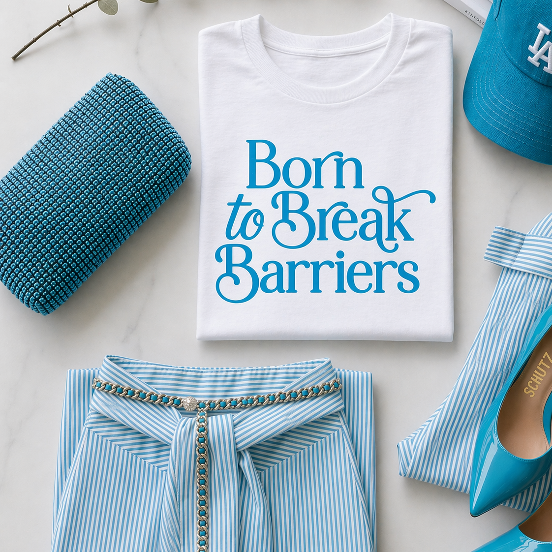 White t-shirt with 'Born to Break Barriers' text, blue striped shirt, blue shoes, and blue clutch on a light background.