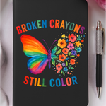 Black notebook with a colorful butterfly design and text 'Broken Crayons Still Color' on a white background.