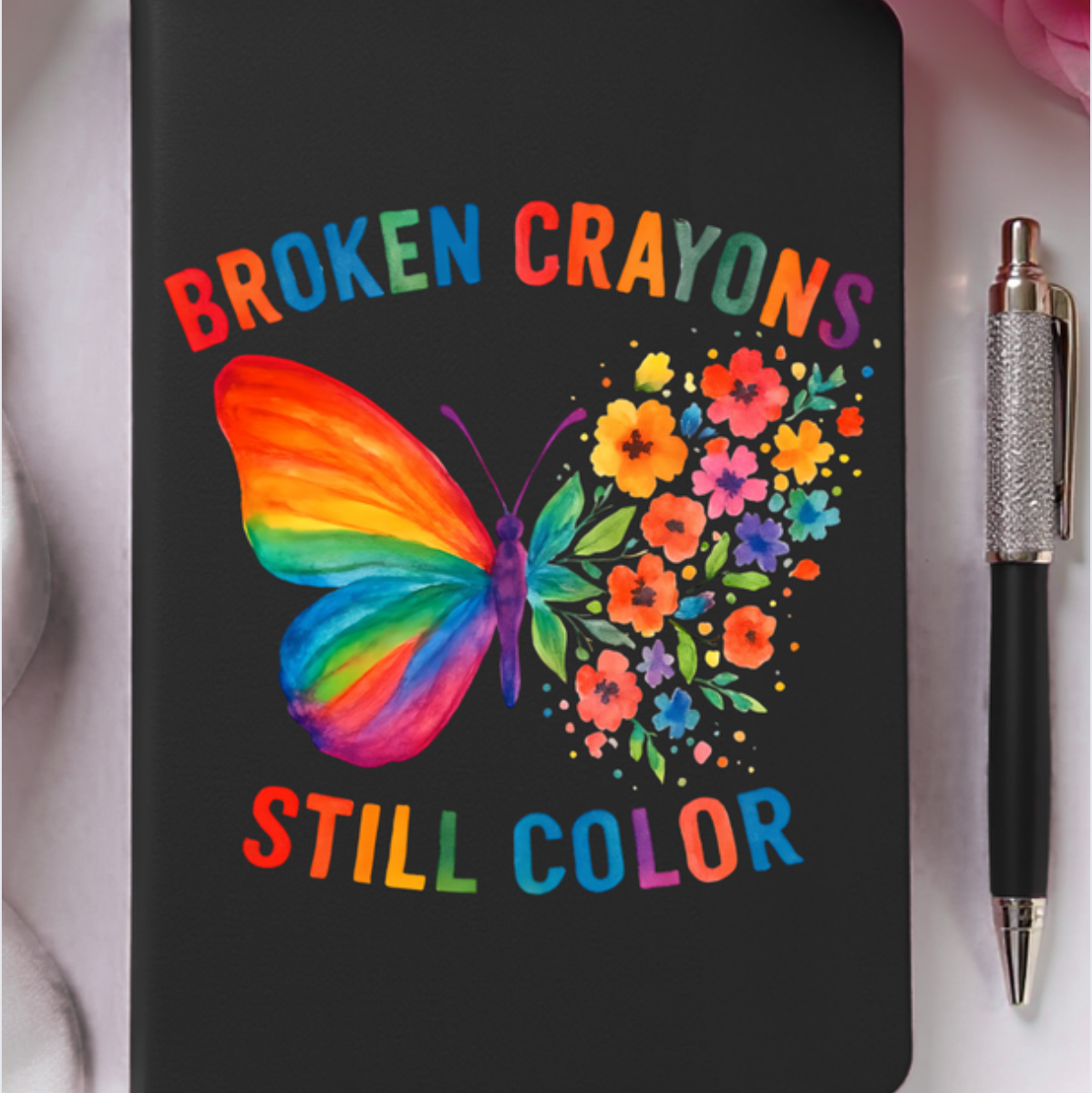 Black notebook with a colorful butterfly design and text 'Broken Crayons Still Color' on a white background.