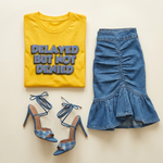 Yellow t-shirt with 'DELAYED BUT NOT DENIED' text, blue denim skirt, and matching shoes on a beige background
