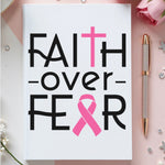 Notebook with 'Faith over Fear' text and pink ribbon on a decorative background with flowers and a pen.