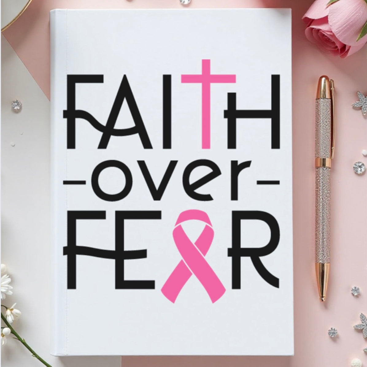 Notebook with 'Faith over Fear' text and pink ribbon on a decorative background with flowers and a pen.