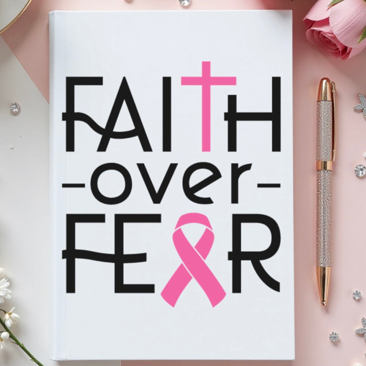 Notebook with 'Faith over Fear' text and pink ribbon on a decorative background with flowers and a pen.