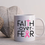 White mug with 'Faith over Fear' text and pink ribbon design on a light background