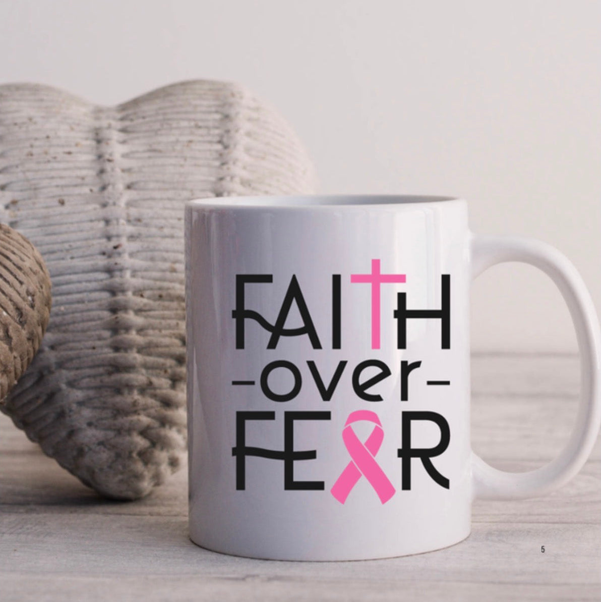 White mug with 'Faith over Fear' text and pink ribbon design on a light background