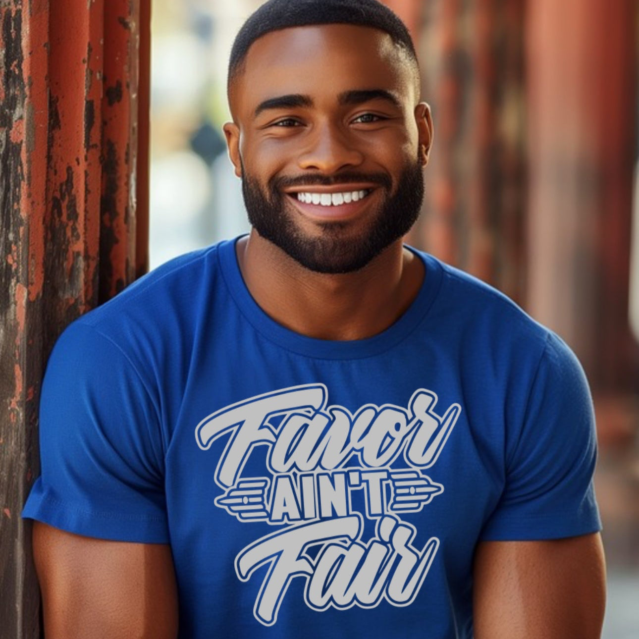 Man wearing a blue t-shirt with text, "FAVOR AIN'T FAIR BLUE" sitting against a textured wall.
