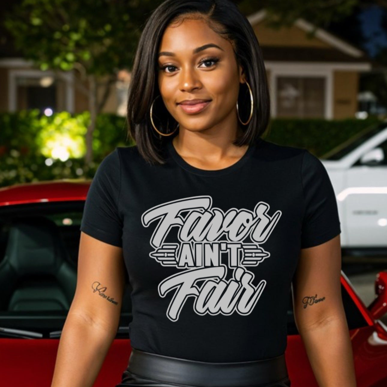 Woman wearing a black t-shirt with text, FAVOR_AIN_T_FAIR_sitting on a red car.