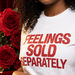Person wearing a white t-shirt with 'FEELINGS SOLD SEPARATELY' text, surrounded by red roses and a newspaper.