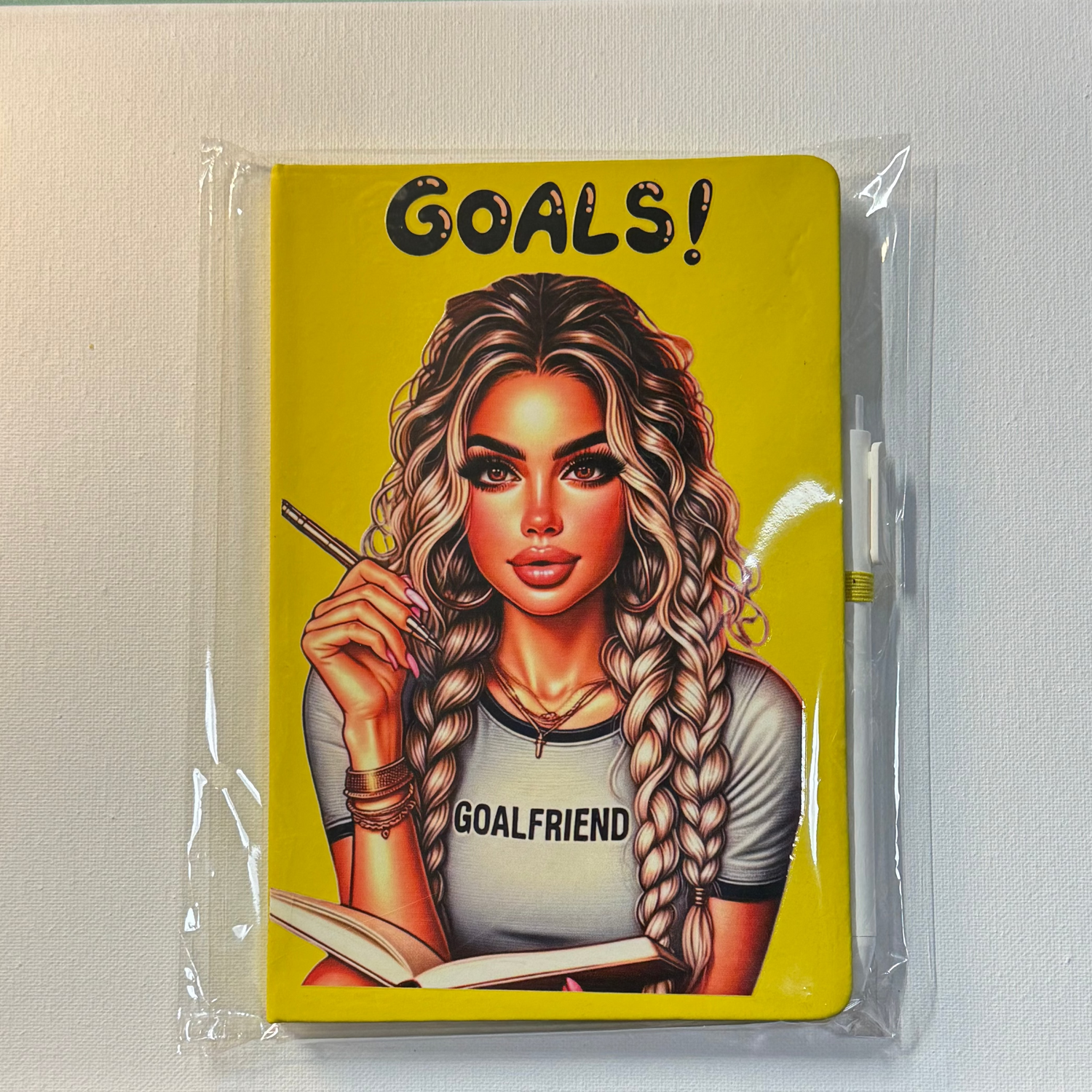 Notebook with an illustration of a woman holding a pencil and a notebook, with 'GOALS!' text on a yellow background.