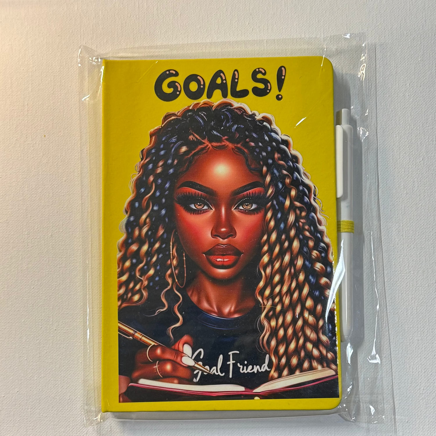 Notebook with a colorful cover featuring a woman's portrait and 'Goals!' text, on a white surface.