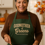 Woman in a kitchen wearing a green apron with 'Godmother of Greens' text, cooking greens.