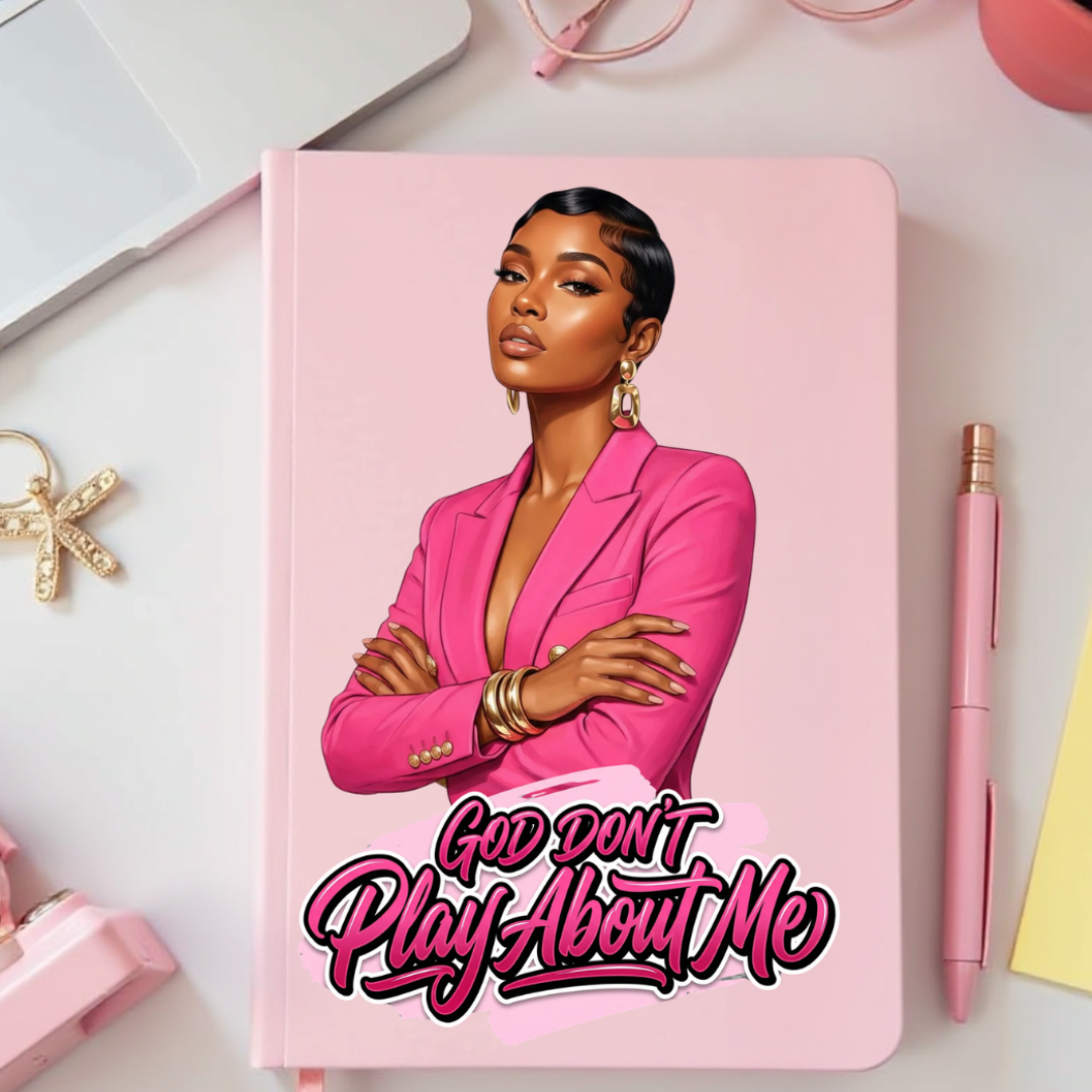 Notebook with a cover featuring a woman in a pink blazer and text 'God Don't Play About Me' on a desk with office supplies.