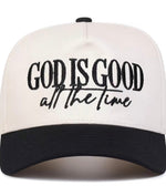 A two-tone baseball cap with an off-white crown and a black curved brim. The front of the cap features black embroidered text that reads 'GOD IS GOOD all the time'.