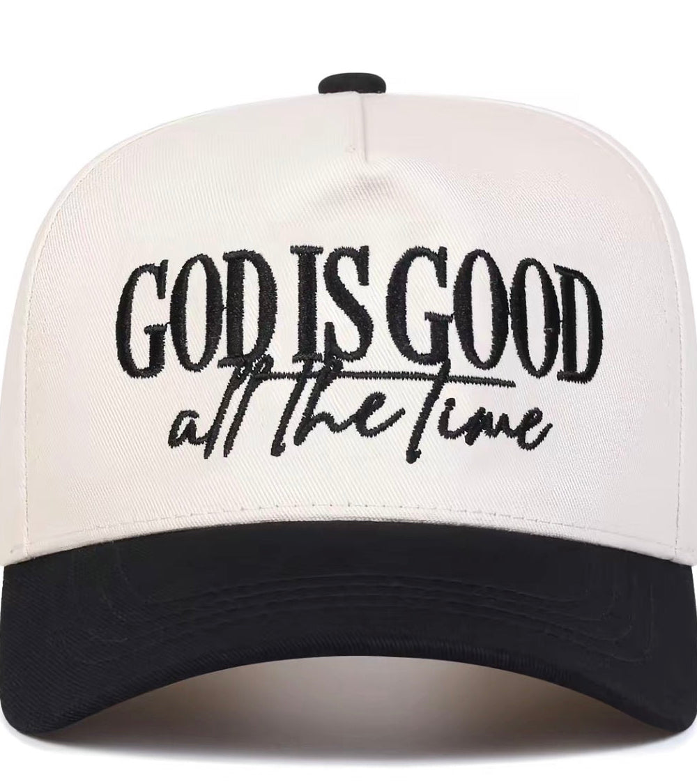 A two-tone baseball cap with an off-white crown and a black curved brim. The front of the cap features black embroidered text that reads 'GOD IS GOOD all the time'.