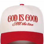 A two-tone trucker-style baseball cap with an off-white crown and a red visor, featuring the embroidered text 'GOD IS GOOD All the time' in red on the front.
