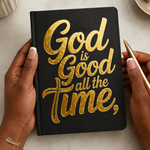 Black notebook with 'God is Good all the time' in gold on a light surface.