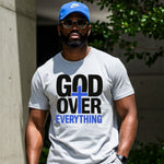 Man wearing a white t-shirt with 'God Over Everything' text and a blue cap outdoors.