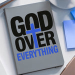 Notebook with 'God Over Everything' text on a desk with a coffee cup and notepad.