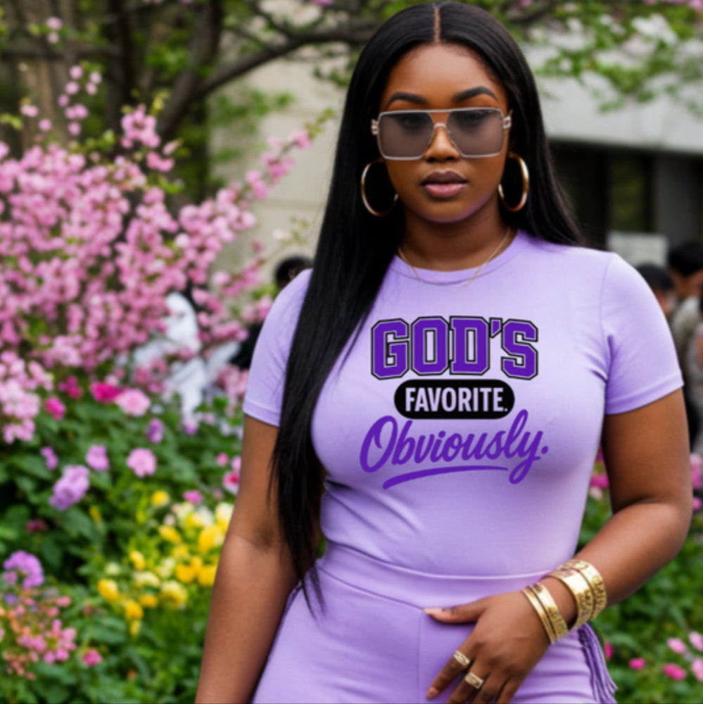 Woman wearing a purple outfit with 'GOD'S FAVORITE Obviously' text, standing in a garden.