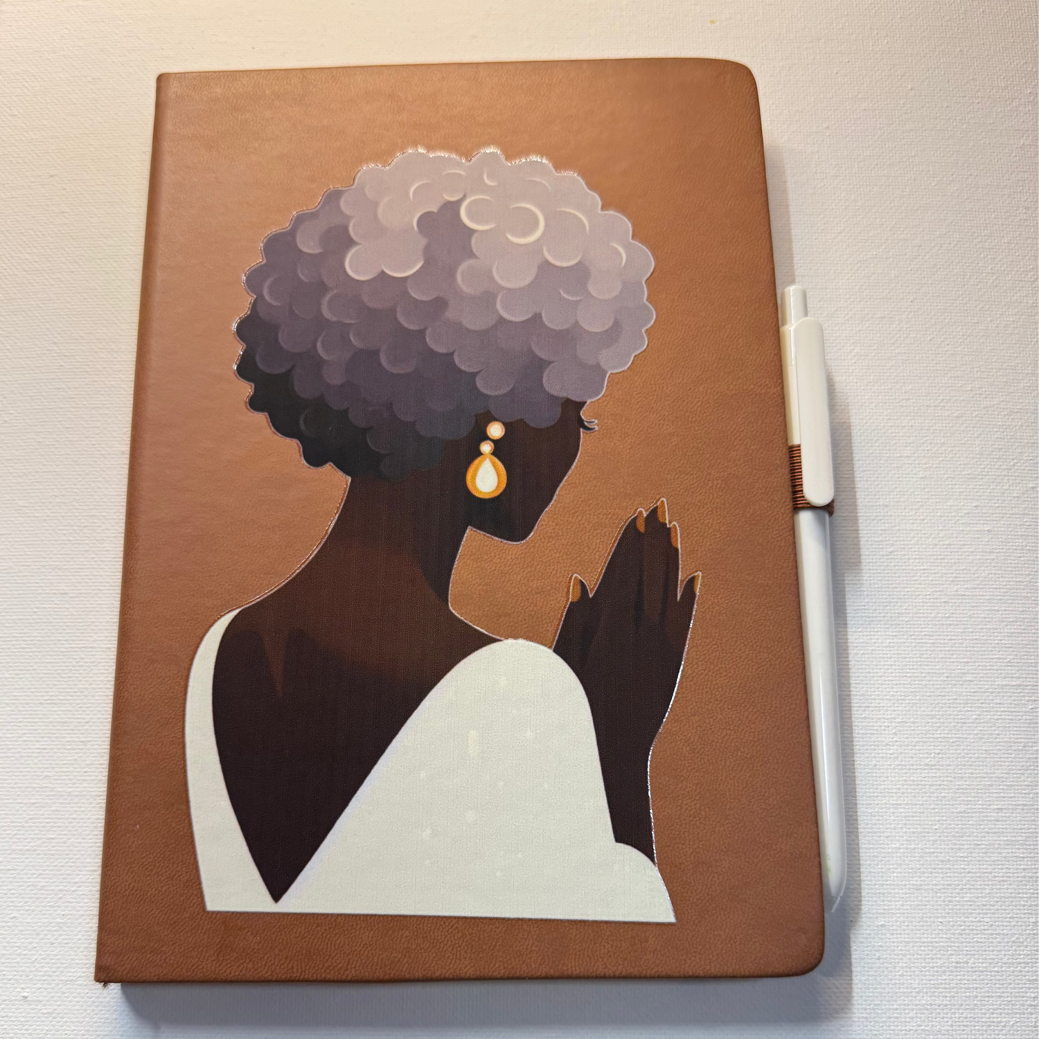 Notebook with a design of a woman with gray hair on a brown cover, placed on a white surface.