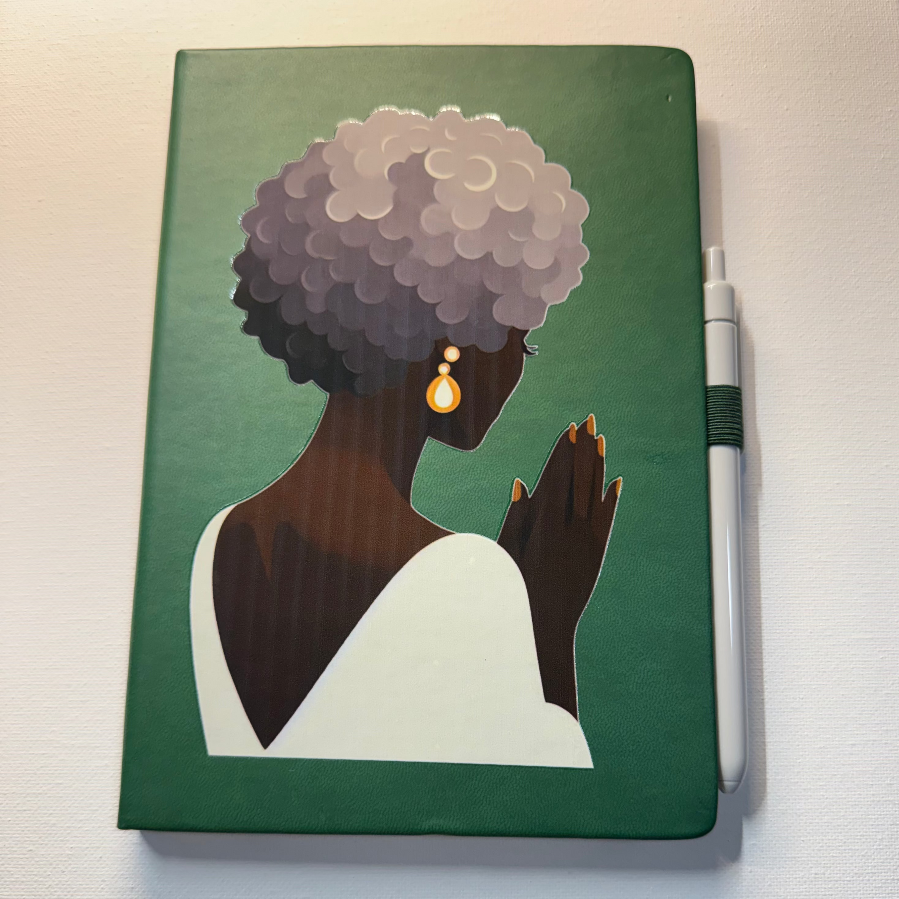 Notebook with a painting of a woman on the cover, placed on a white surface.