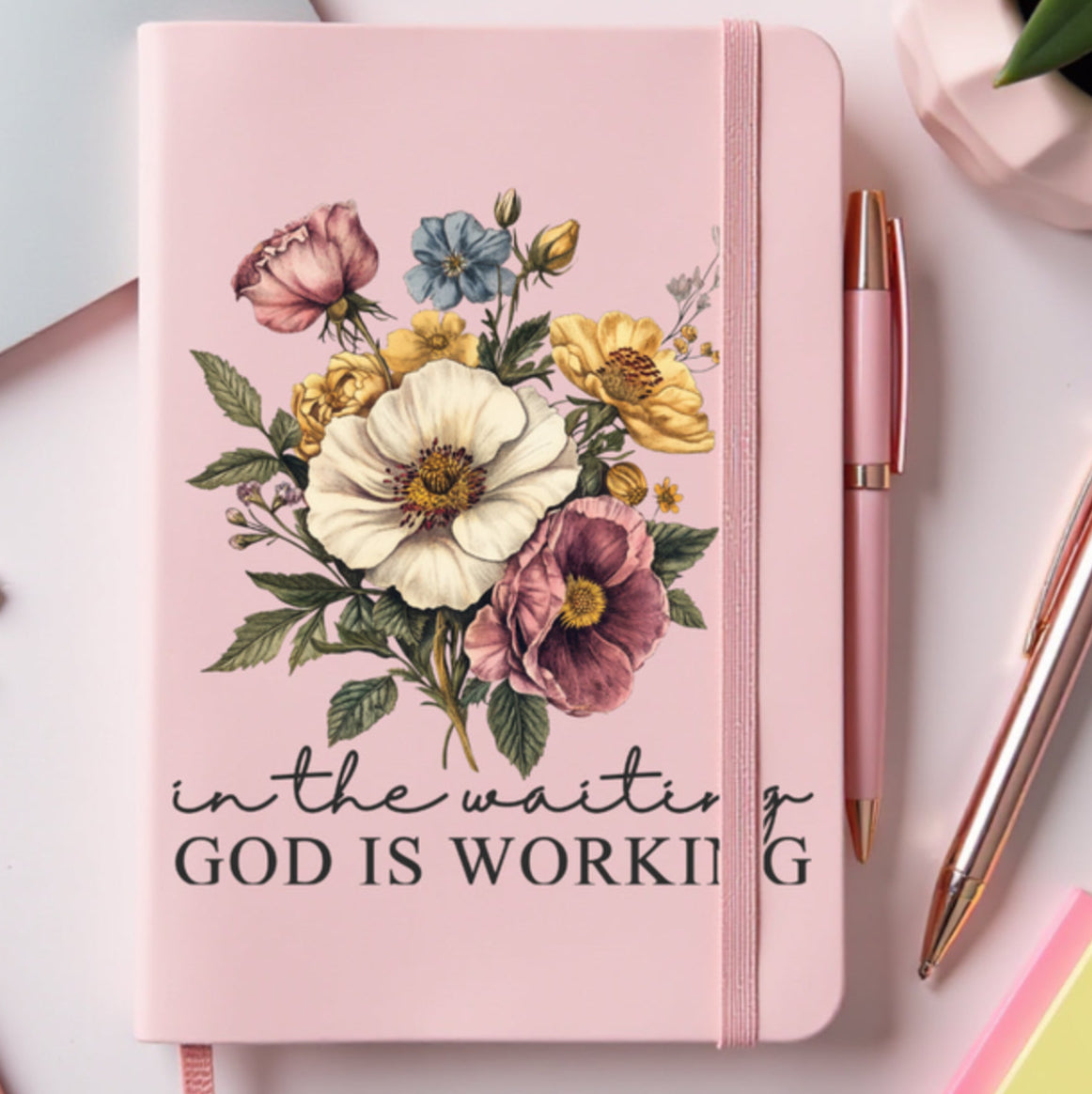 Pink notebook with floral design and text IN THE WAITING GOD IS WORKING.
