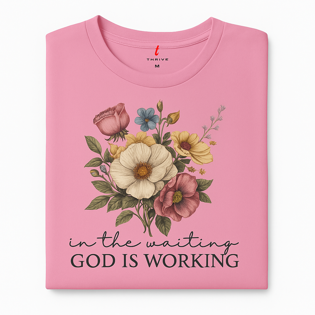 Pink t-shirt with floral design and text 'In the waiting God is working' on a white background