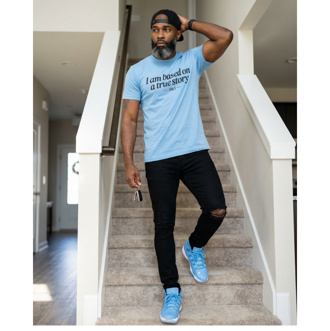 Man wearing a light blue t-shirt with text, black pants, and blue sneakers standing on a staircase.