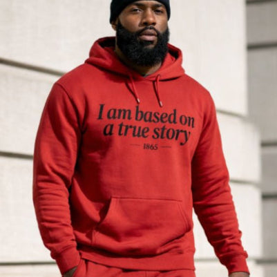 Person wearing a red hoodie and pants with text, standing against a light-colored wall.